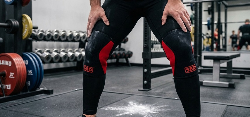 A powerlifter wearing SBD knee sleeves in a well-equipped gym, showcasing the product in a real-world setting.