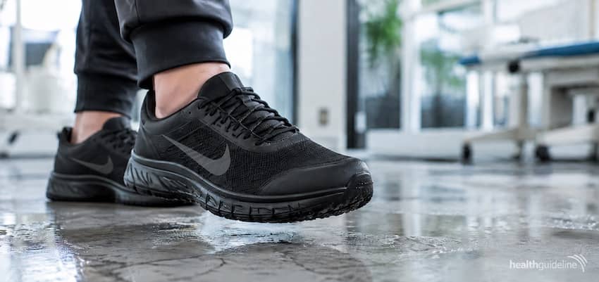 Black Nike slip-resistant shoes worn on a wet, reflective floor, highlighting the textured outsole and secure traction design.